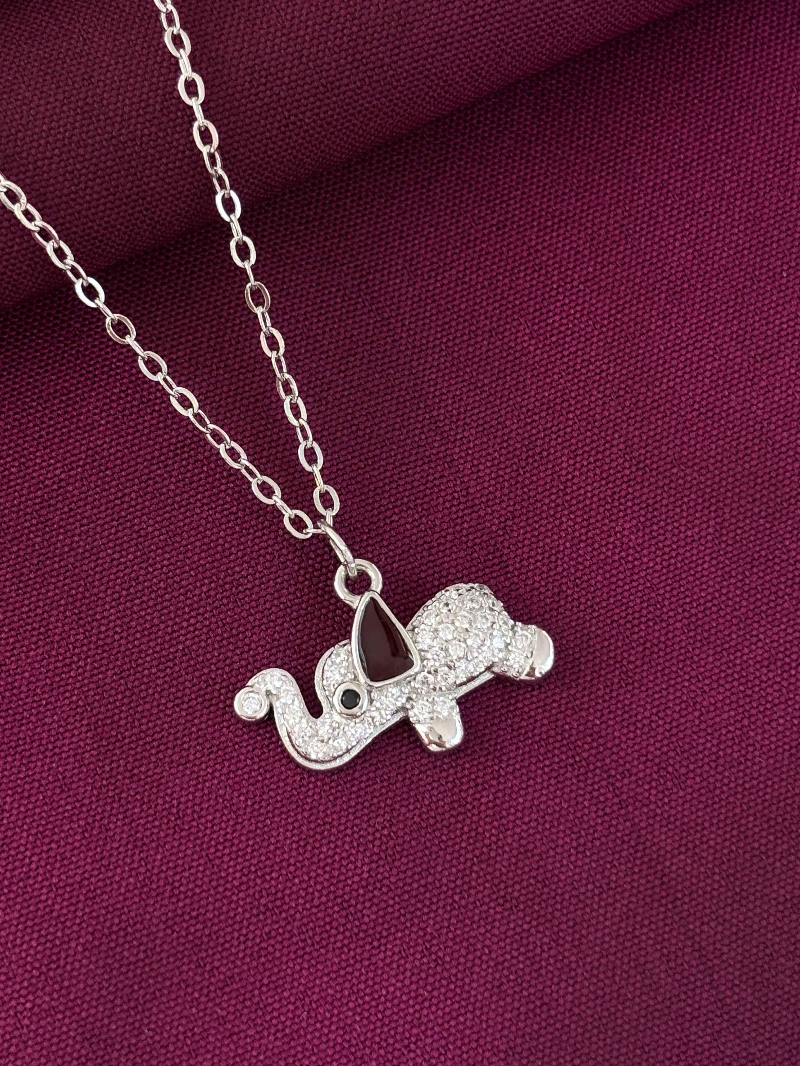 Silver elephant pendant on a chain against a purple fabric background