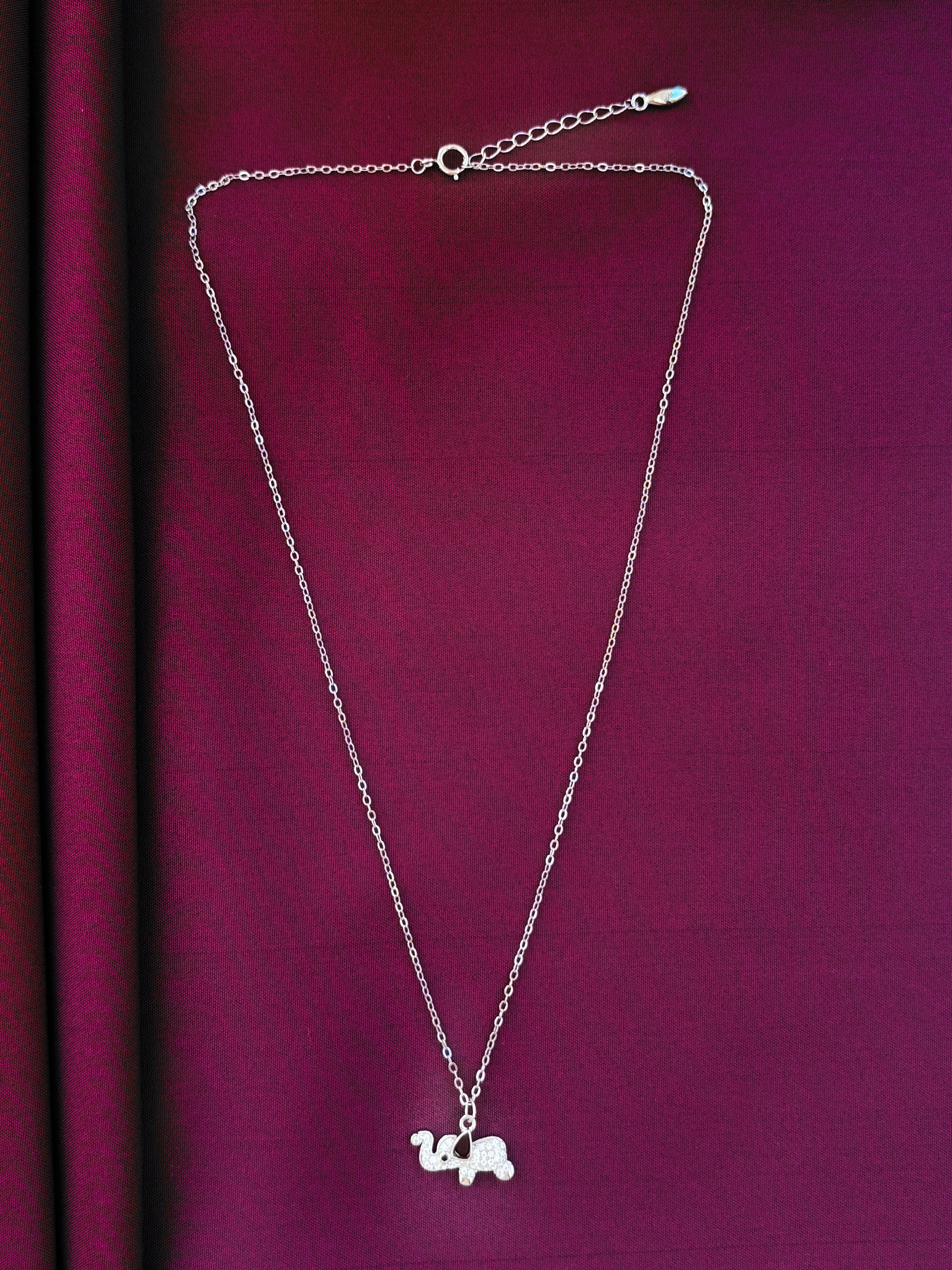 Silver chain pendent with a small pendant on a purple fabric background