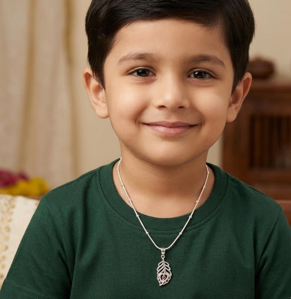 Young boy wearing a green shirt and silver necklace with a pendant, sitting indoors.