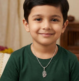 Young boy wearing a green shirt and silver necklace with a pendant, sitting indoors.