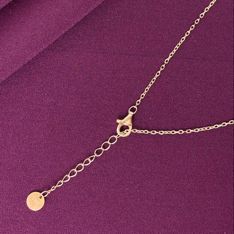 Gold necklace with a small round pendant on a purple fabric background