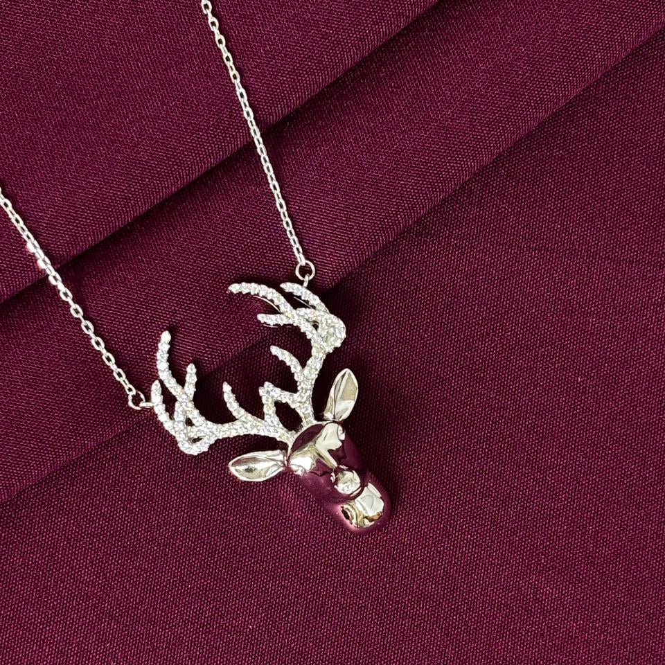 Silver deer head necklace on a burgundy fabric background