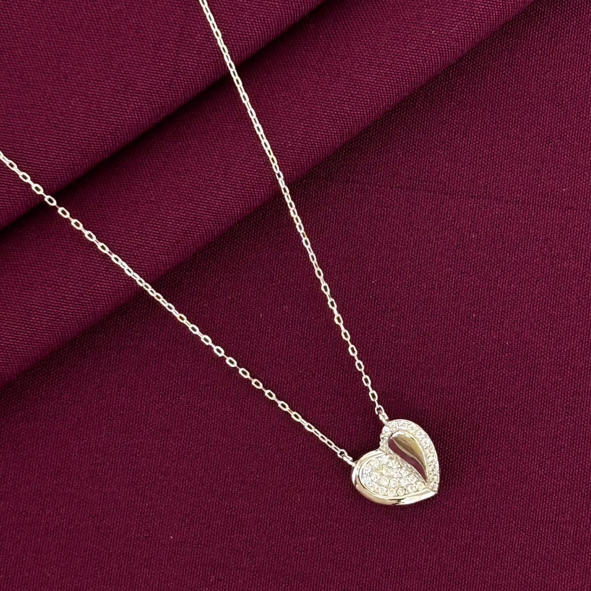 Heart-shaped pendant necklace on a burgundy fabric background