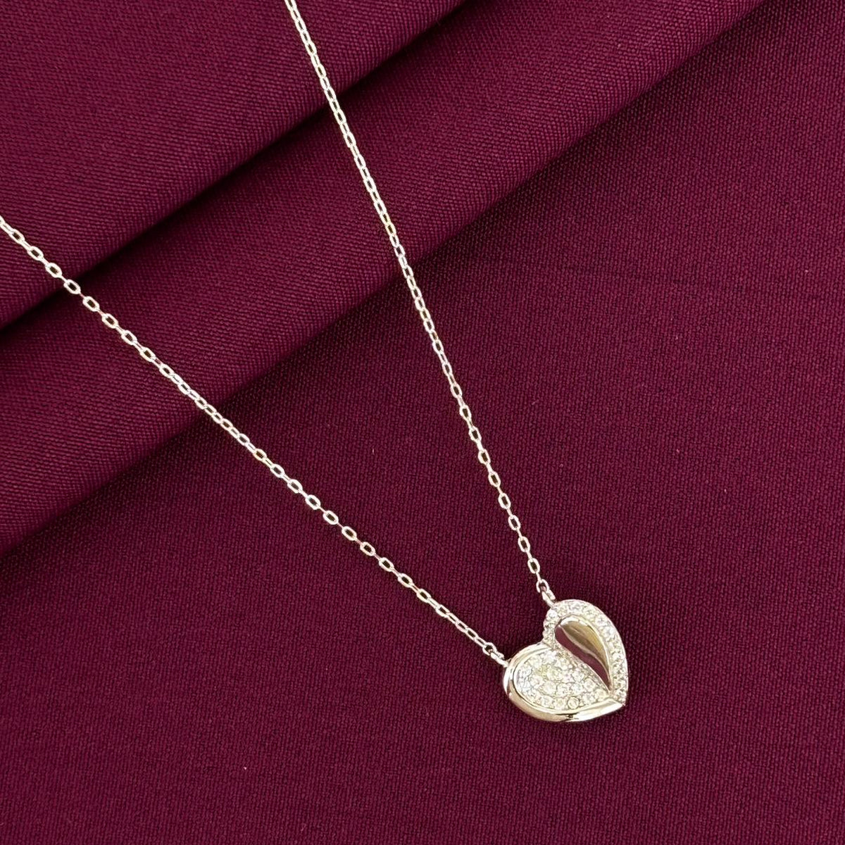 Heart-shaped pendant necklace on a burgundy fabric background